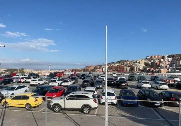 Amplio aparcamiento de coches en bsm Sant Genís, con la ciudad al fondo bajo un cielo azul.
