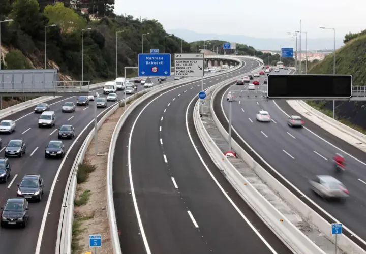Autopista con varios carriles, incluyendo un carril Vao, con tráfico de coches y furgonetas. Señales de tráfico indican direcciones.