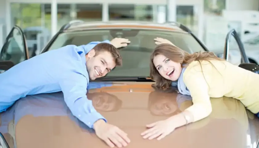 Pareja feliz abraza su nuevo coche, demostrando que se puede poner un coche a nombre de dos personas.