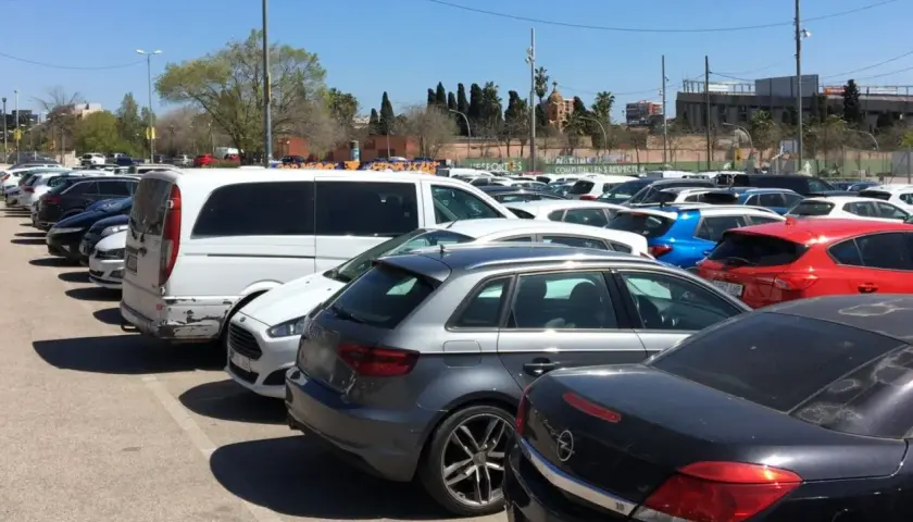 Amplio aparcamiento gratuito en el aeropuerto de Barcelona, con coches de diversos colores y modelos bajo un cielo azul.