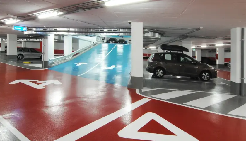 Estacionamiento subterráneo con señalización de salida y flechas en el suelo. Un coche oscuro con portaequipajes bsm flos i calcat.