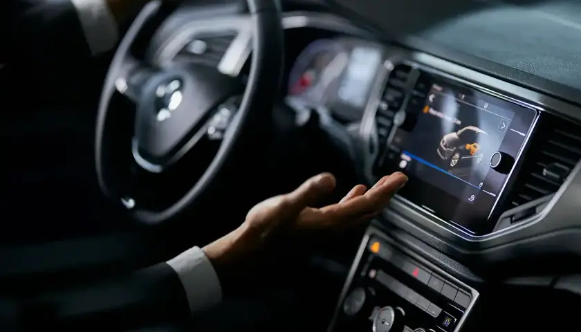 Mano interactuando con la pantalla táctil de un coche, mostrando el futuro de los coches autónomos.