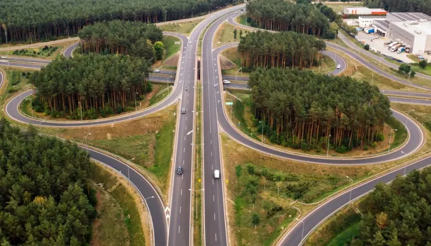 Un cruce de autopistas con un carril trenzado serpentea entre bosques de pinos.