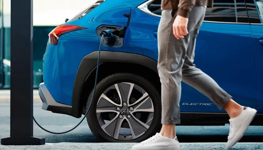Un coche azul eléctrico se carga mientras una persona camina. Así es un phev que es, híbrido enchufable.