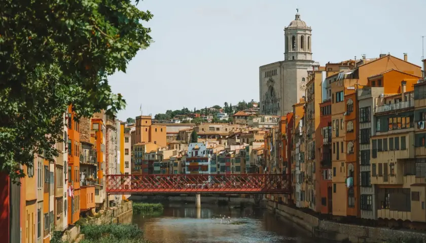 Casas de colores junto al río Onyar y el puente de piedra roja. La catedral se alza al fondo. Una vista encantadora para saber cómo llegar a Girona.
