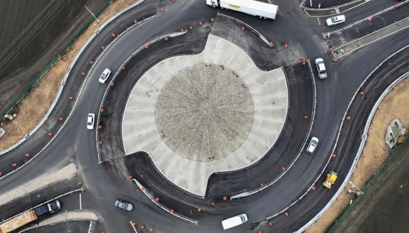 Vista aérea de una turbo rotonda en construcción, con coches circulando y un rodillo amarillo trabajando.