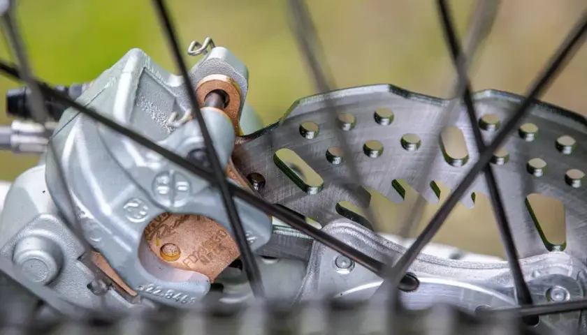 Primer plano de un freno de disco de bicicleta con pastillas de freno gastadas. El disco metálico muestra signos de uso, y las pastillas de freno están desgastadas.