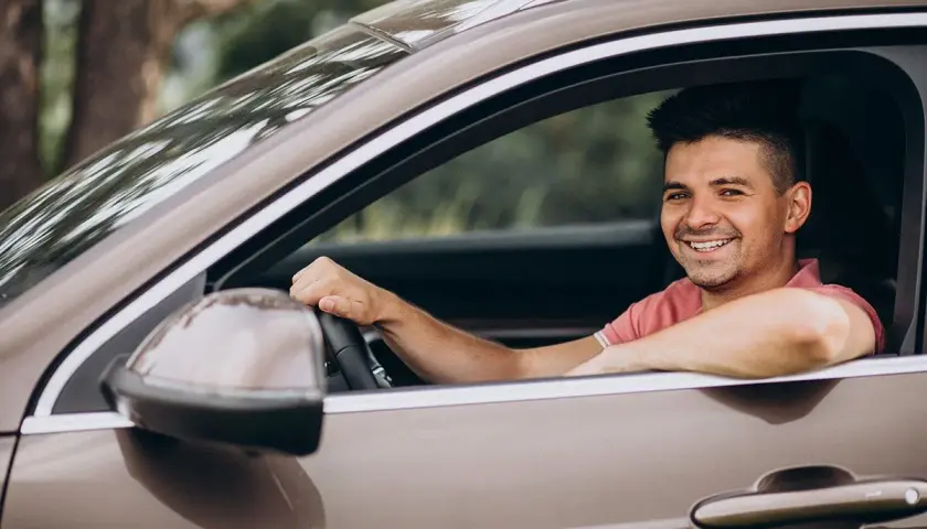 Hombre sonriente al volante, disfrutando de un viaje. La pregunta sobre hasta qué edad se puede conducir en España es relevante para muchos.