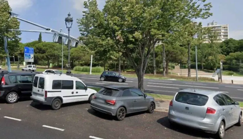 Coches aparcados en zonas blancas de Barcelona, junto a un parque y una carretera.