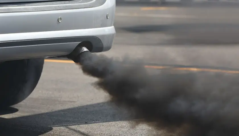 El tubo de escape de un coche emite humo negro denso, sugiriendo un fuerte olor a quemado de coche.