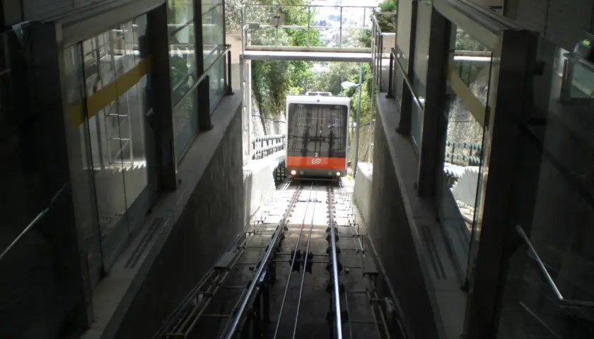 El funicular de Vallvidrera desciende por las vías entre estructuras de vidrio y hormigón, con vegetación al fondo.