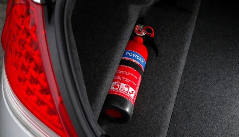 Extintor rojo en el maletero de un coche, listo para usar. Es obligatorio llevar extintor en el coche para tu seguridad.