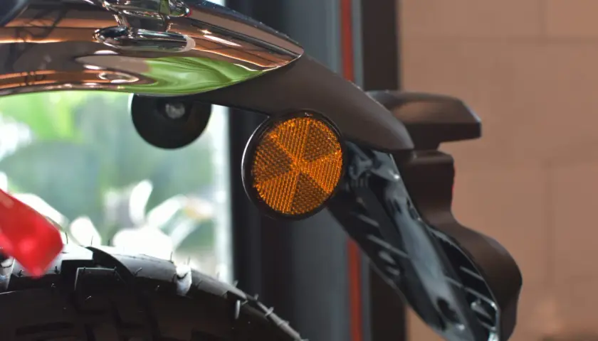 Detalle de una moto con un catadióptrico naranja que refleja la luz, aumentando la seguridad.