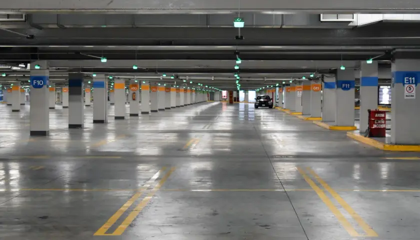 Estacionamiento subterráneo con luces verdes, columnas numeradas y un coche negro. Líneas amarillas marcan los espacios. ¡Encuentra tu lugar de parking gratis!