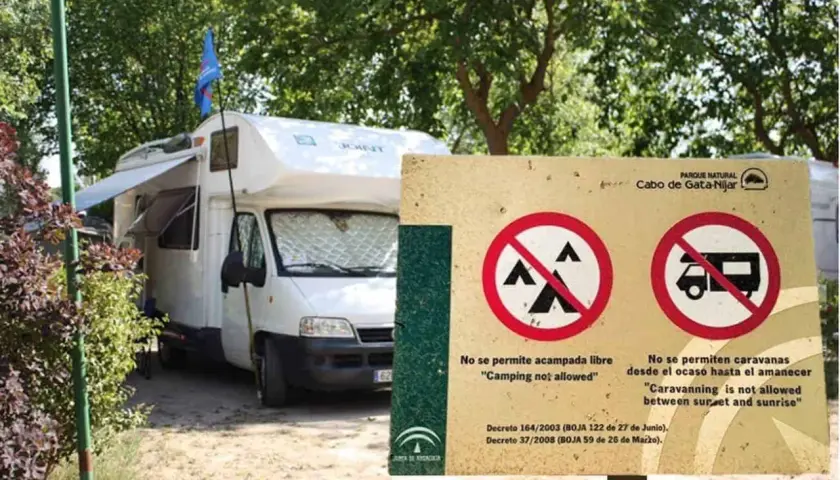 Una autocaravana blanca está aparcada junto a un cartel que prohíbe acampar y aparcar caravanas de noche.
