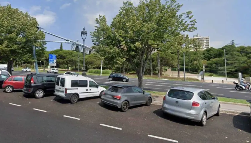 Varios coches aparcados en el parking del Hospital del Mar, con árboles y edificios al fondo.