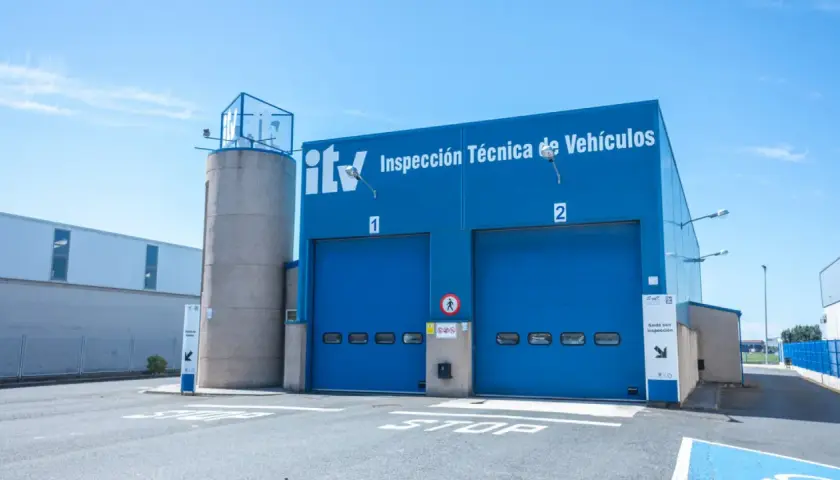 Edificio azul de ITV con dos puertas de garaje. Un coche listo para pasar la primera ITV.