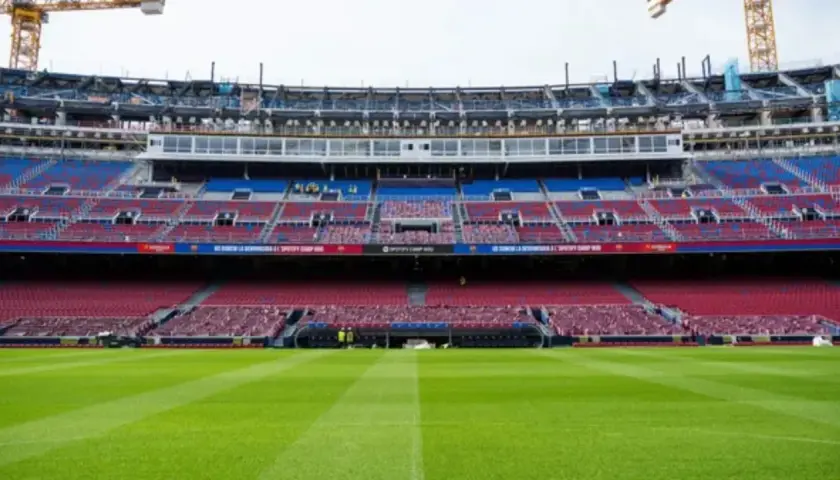 El estadio Spotify Camp Nou en obras, con grúas visibles. Las gradas rojas y azules esperan a los aficionados tras la renovación, cerca de la estación de metro.