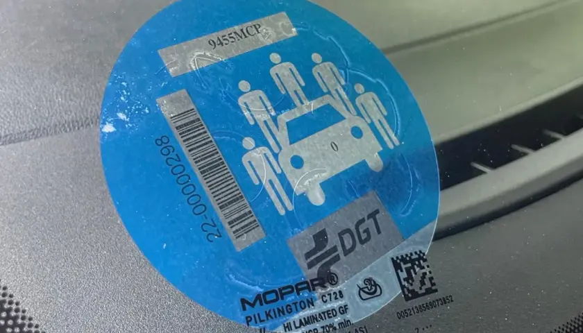 Pegatina azul con siluetas de personas y un coche, indicando la **señal v26**. Muestra un código de barras y el logo de DGT.