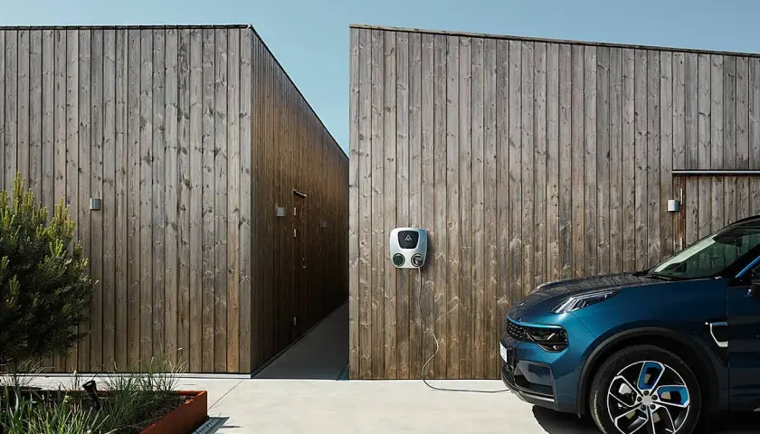 Coche azul conectado a uno de los puntos de recarga en una pared de madera.