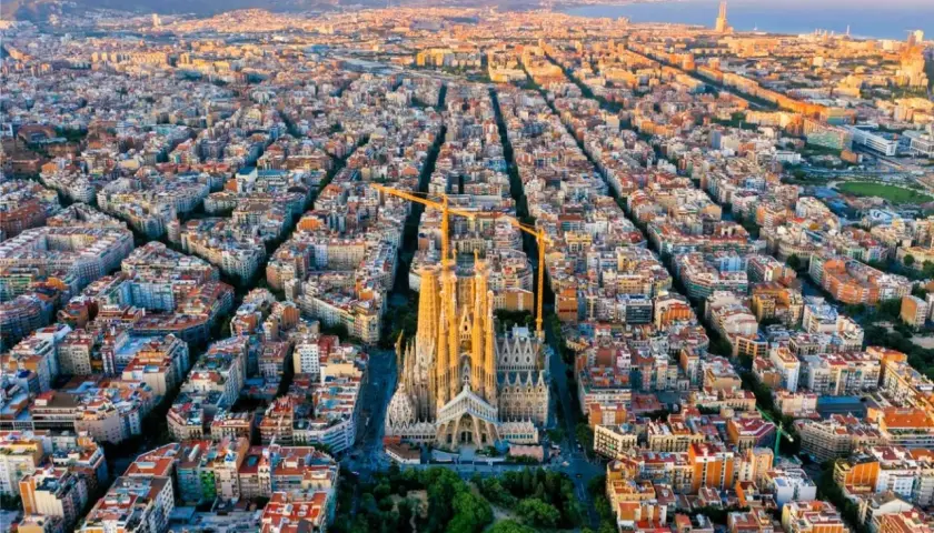 Vista aérea de Barcelona al atardecer, con la Sagrada Familia como punto focal. Las grúas de construcción rodean la basílica, símbolo de la ciudad.