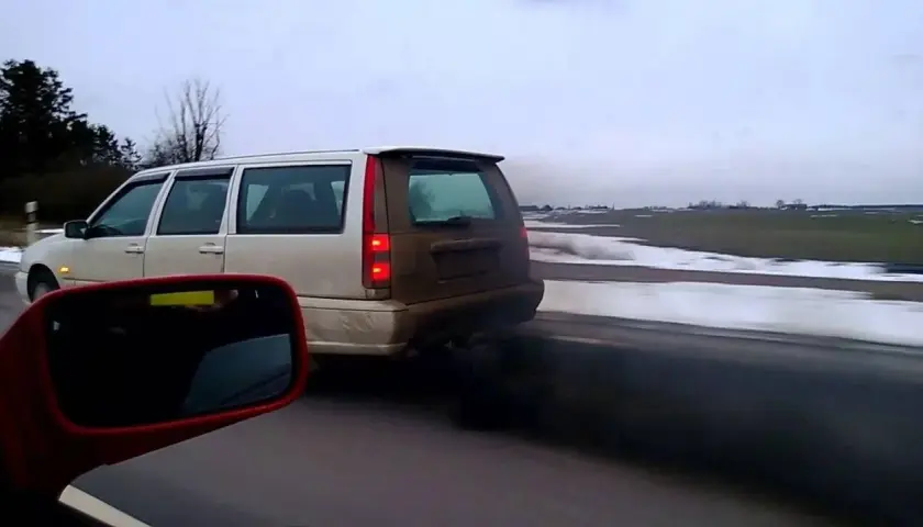 Un coche emite una densa nube de humo negro mientras circula por una carretera nevada.