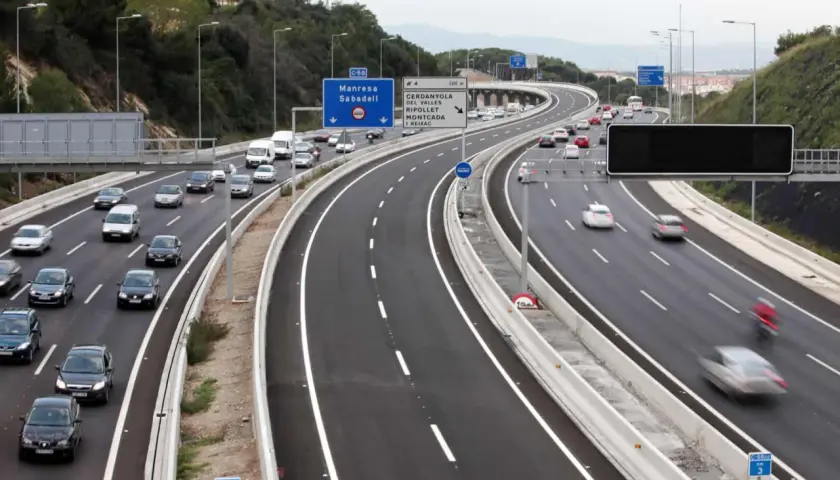 Autopista con varios carriles, incluyendo un carril Vao, con tráfico de coches y furgonetas. Señales de tráfico indican direcciones.