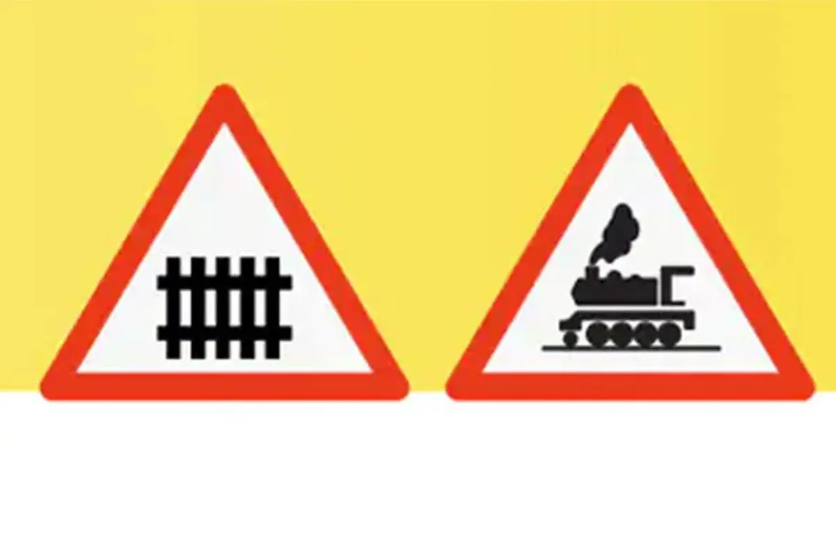 Dos señales de advertencia triangulares con borde rojo sobre fondo amarillo. Una muestra vías de tren, la otra una locomotora. Indican un paso a nivel con barreras.