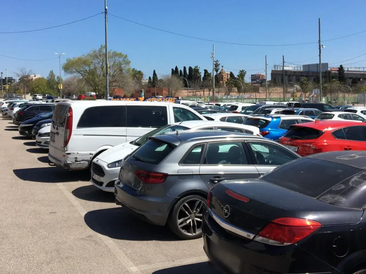 Amplio aparcamiento gratuito en el aeropuerto de Barcelona, con coches de diversos colores y modelos bajo un cielo azul.