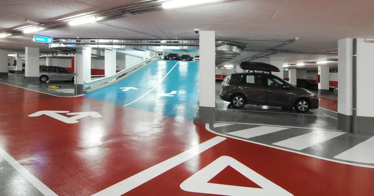 Estacionamiento subterráneo con señalización de salida y flechas en el suelo. Un coche oscuro con portaequipajes bsm flos i calcat.