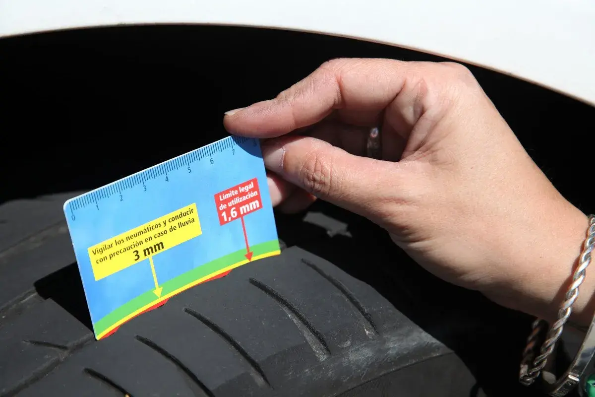 Mano mide la profundidad del dibujo de un neumático con una regla. Indica 3 mm y el límite legal de 1,6 mm, sugiriendo revisar la fecha caducidad neumáticos.