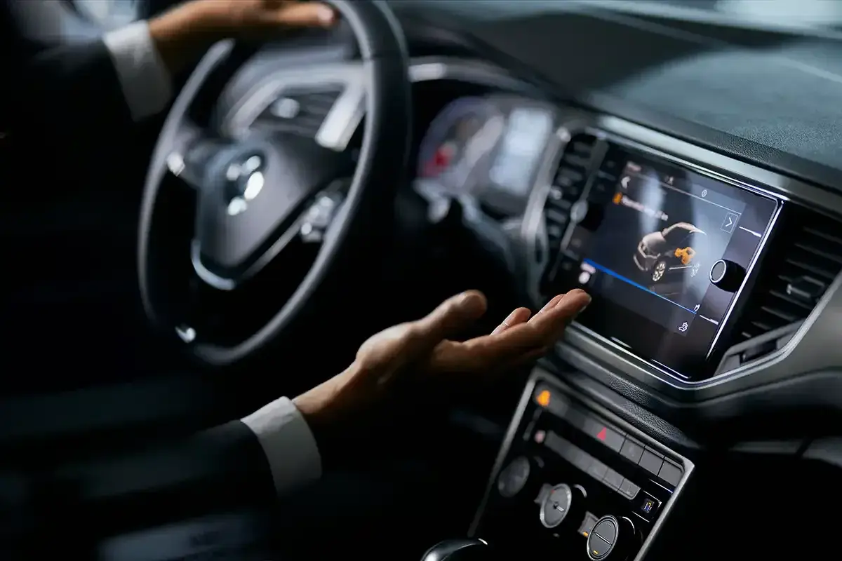Mano interactuando con la pantalla táctil de un coche, mostrando el futuro de los coches autónomos.