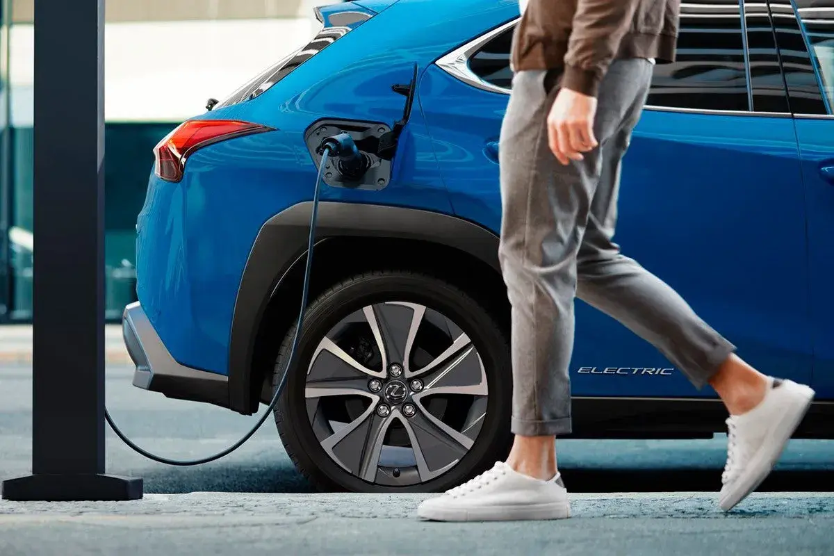 Un coche azul eléctrico se carga mientras una persona camina. Así es un phev que es, híbrido enchufable.