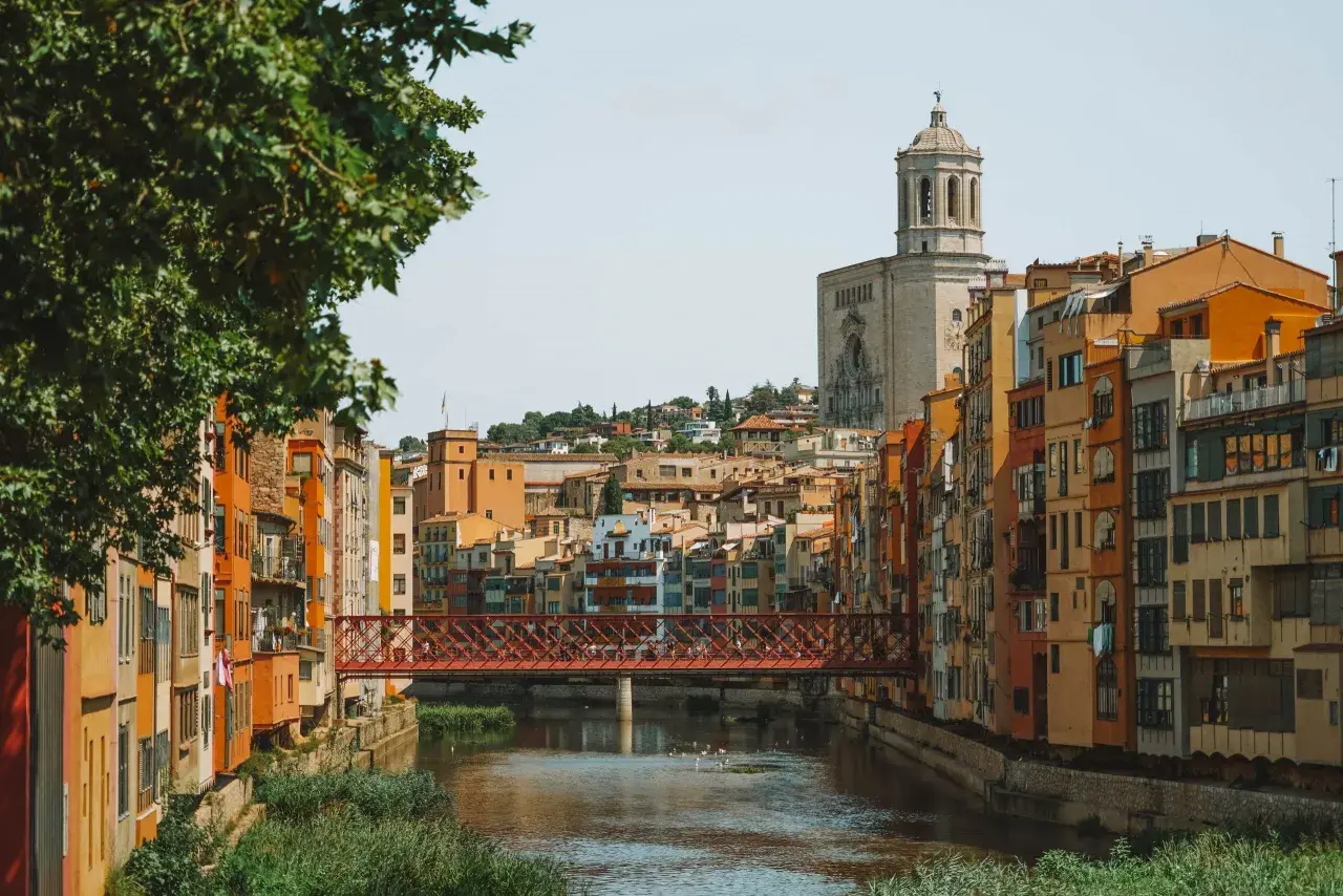 Casas de colores junto al río Onyar y el puente de piedra roja. La catedral se alza al fondo. Una vista encantadora para saber cómo llegar a Girona.