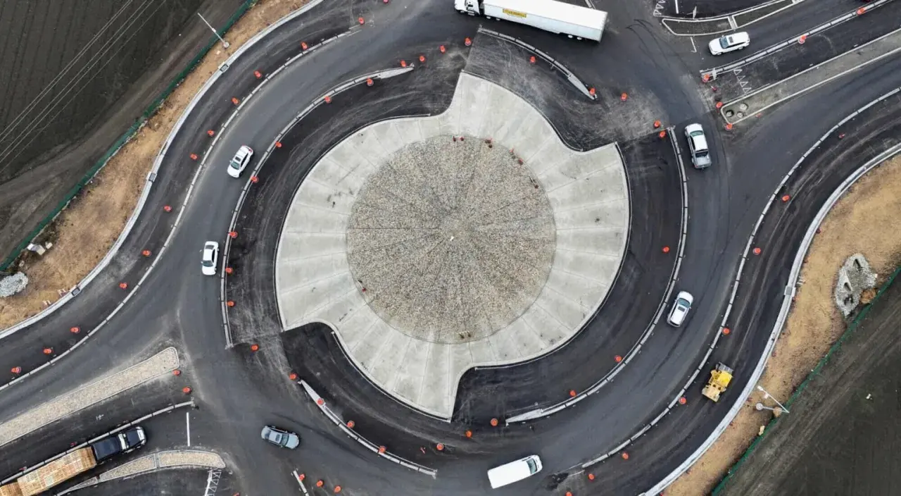 Vista aérea de una turbo rotonda en construcción, con coches circulando y un rodillo amarillo trabajando.