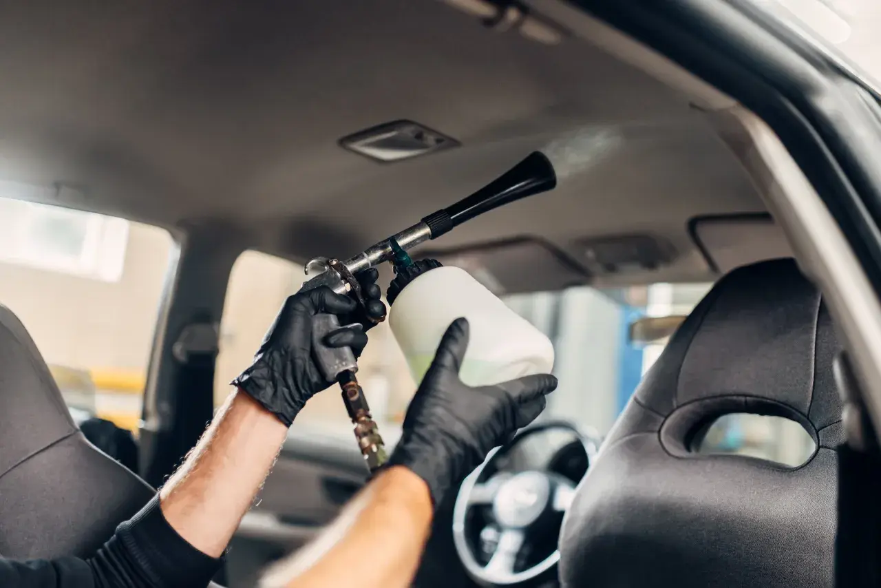 Man con guantes negros usa una pistola de espuma para limpiar el techo del coche.