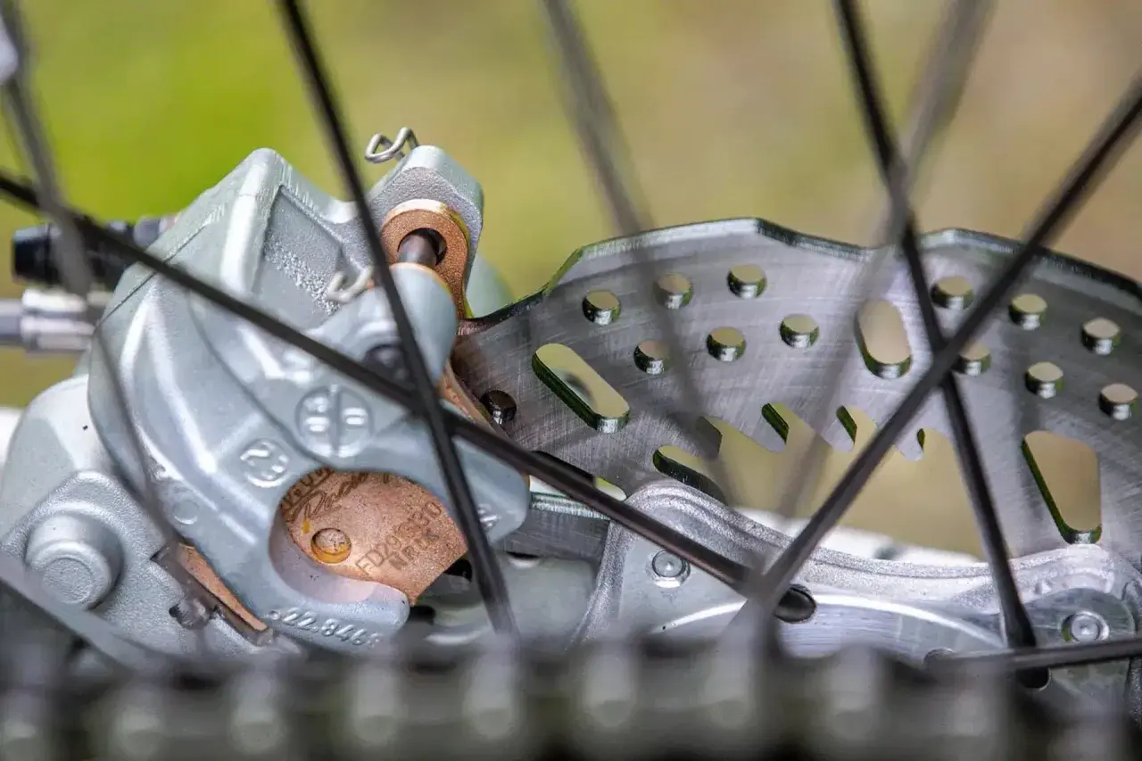 Primer plano de un freno de disco de bicicleta con pastillas de freno gastadas. El disco metálico muestra signos de uso, y las pastillas de freno están desgastadas.