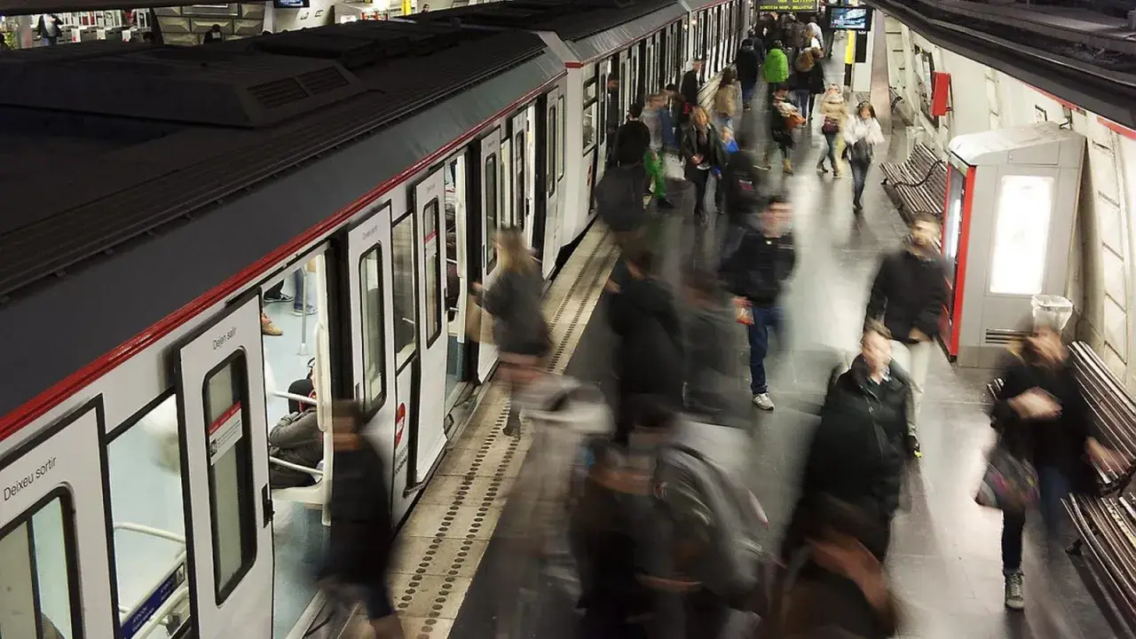 Gente abordando un tren en una estación de metro, con el movimiento borroso sugiriendo la actividad constante de las obras del metro de Barcelona.