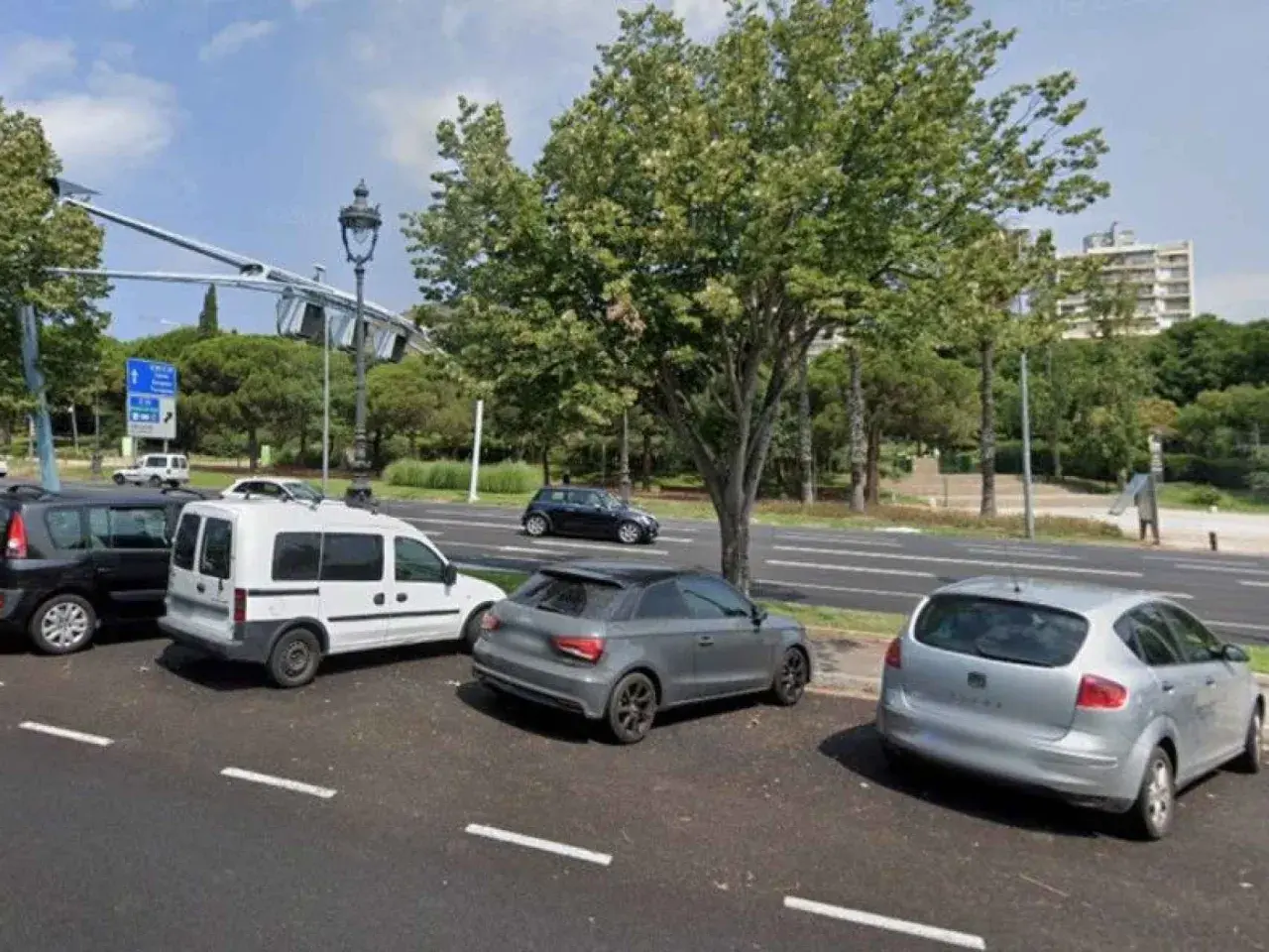 Coches aparcados en zonas blancas de Barcelona, junto a un parque y una carretera.