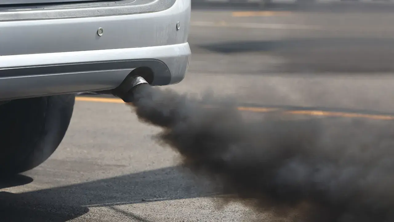 El tubo de escape de un coche emite humo negro denso, sugiriendo un fuerte olor a quemado de coche.