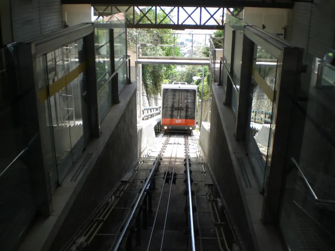 El funicular de Vallvidrera desciende por las vías entre estructuras de vidrio y hormigón, con vegetación al fondo.