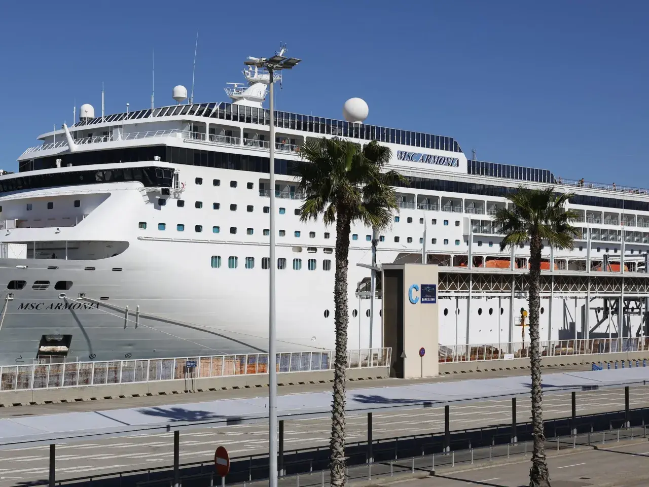 El crucero MSC Armonia atracado en la terminal de cruceros Barcelona, con palmeras y cielo azul.