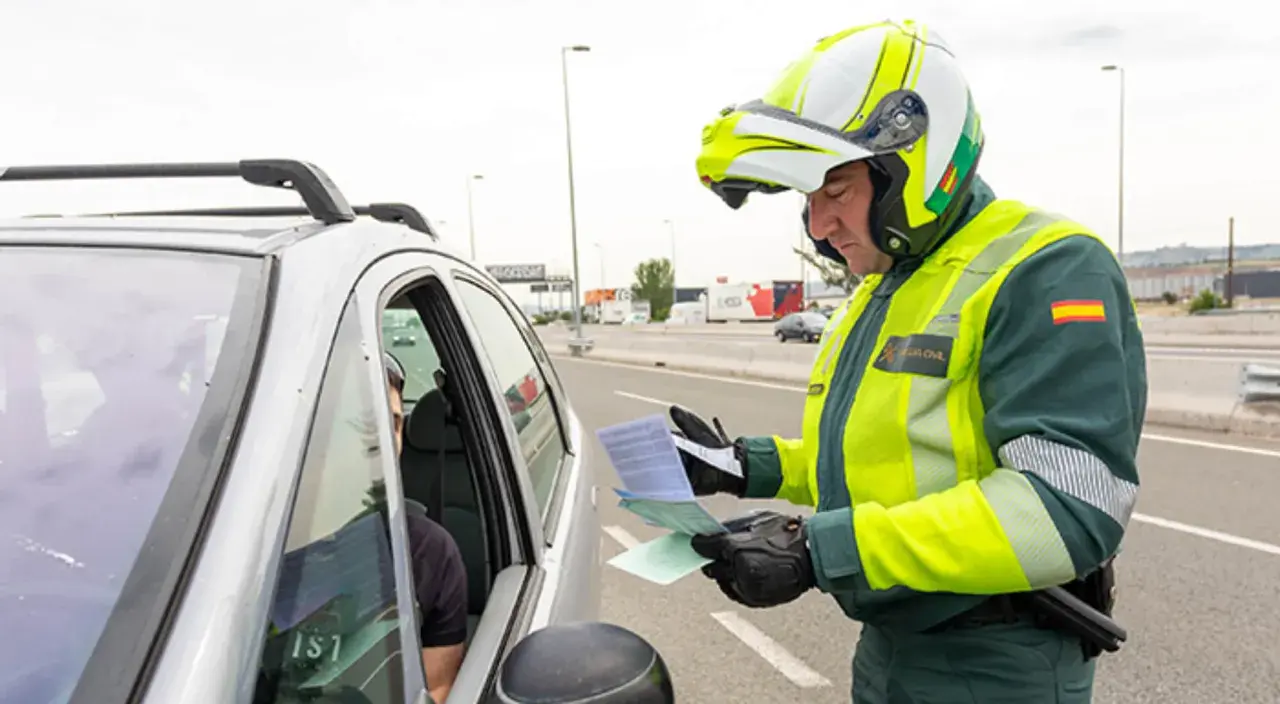 Agente de la Guardia Civil, con casco y chaleco reflectante, se acerca a un coche para entregar un documento. Parece que prescribe una multa.