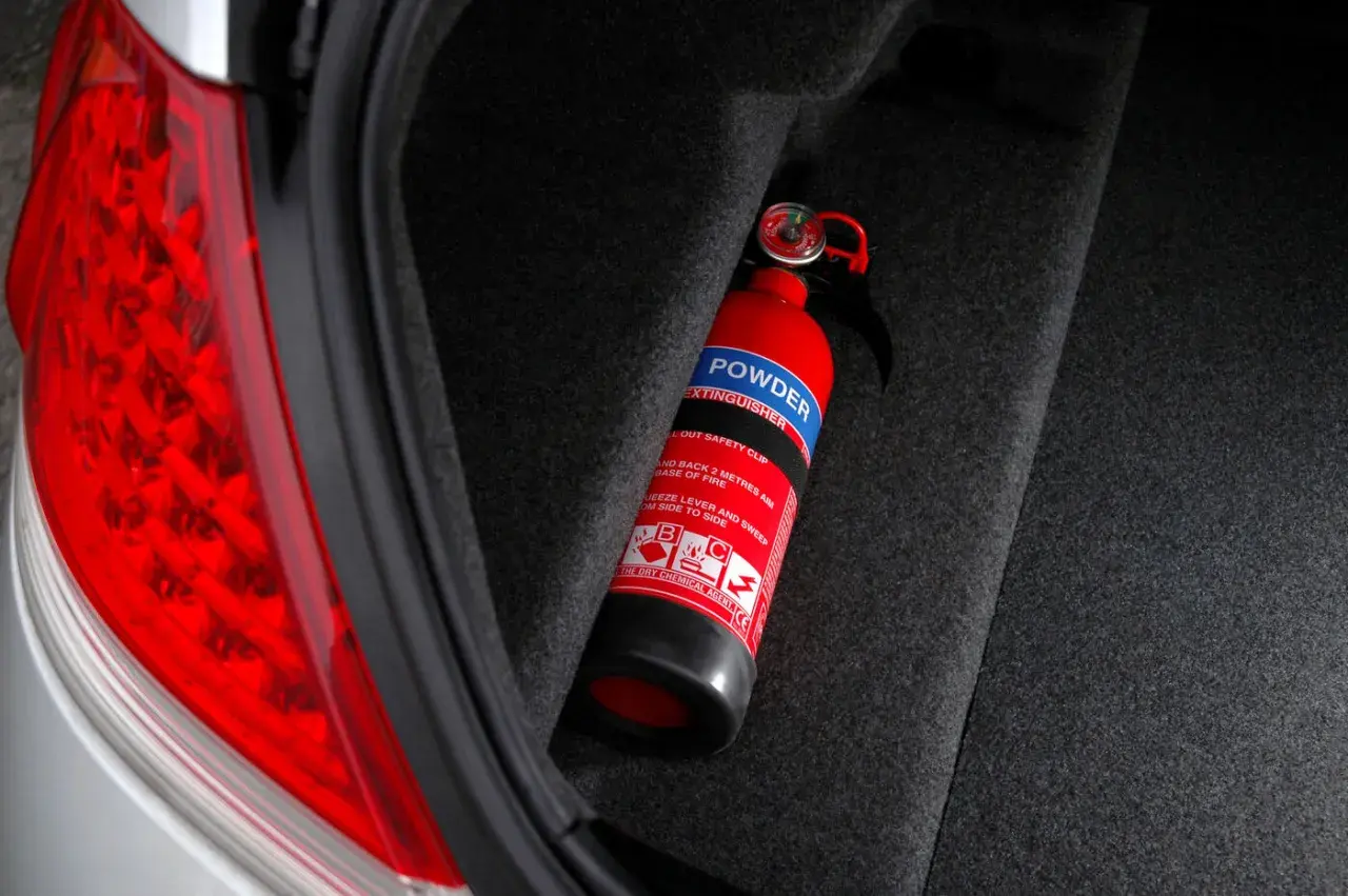Extintor rojo en el maletero de un coche, listo para usar. Es obligatorio llevar extintor en el coche para tu seguridad.