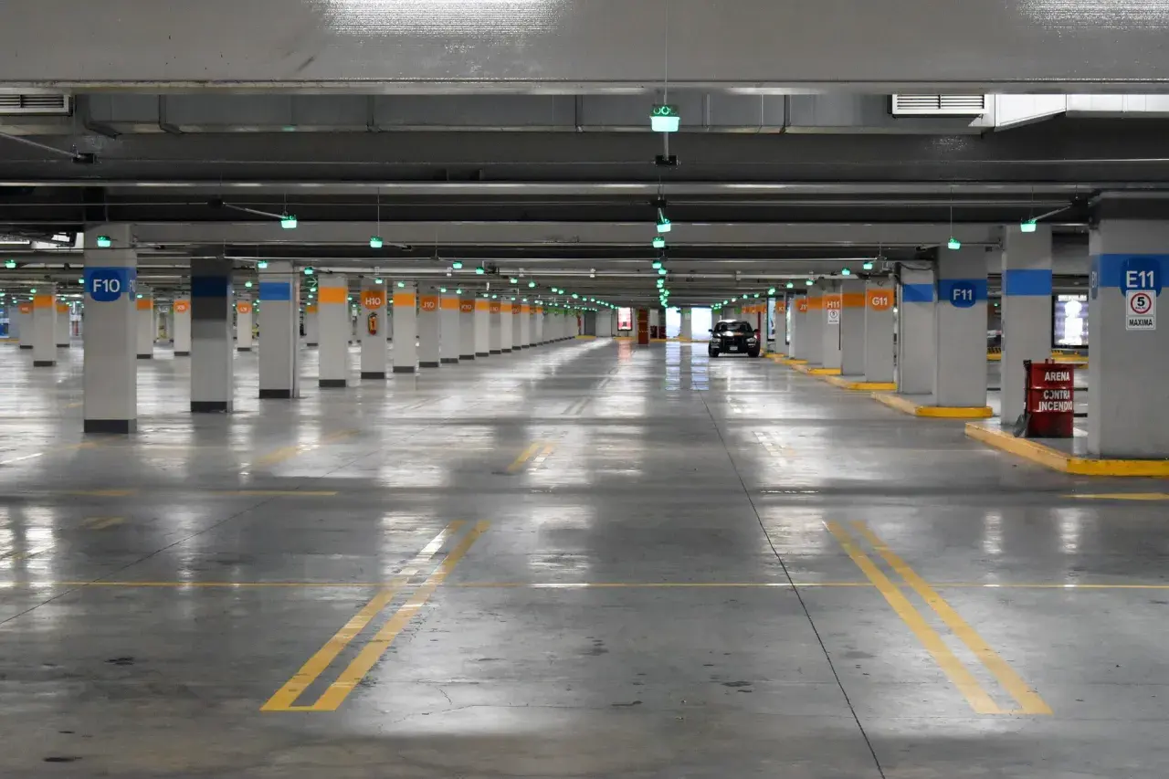 Estacionamiento subterráneo con luces verdes, columnas numeradas y un coche negro. Líneas amarillas marcan los espacios. ¡Encuentra tu lugar de parking gratis!