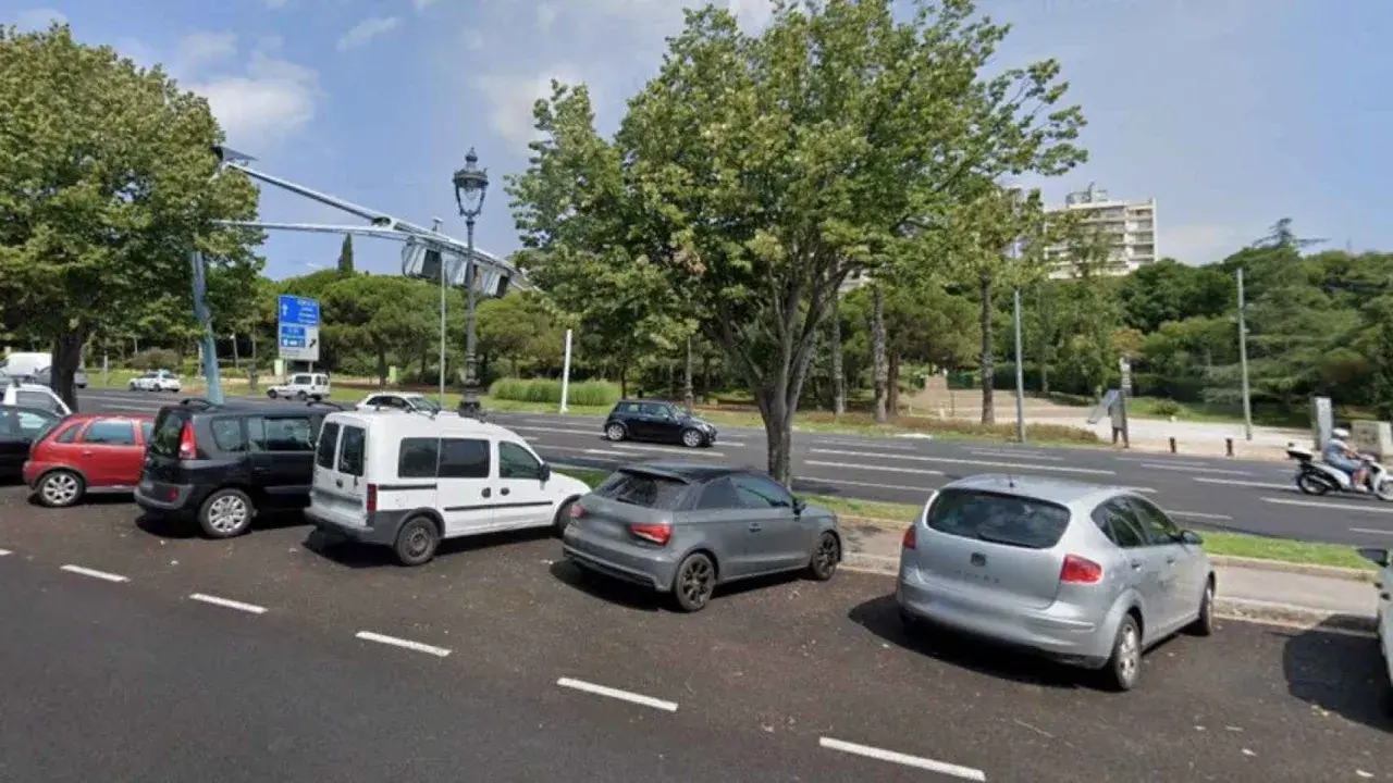 Varios coches aparcados en el parking del Hospital del Mar, con árboles y edificios al fondo.
