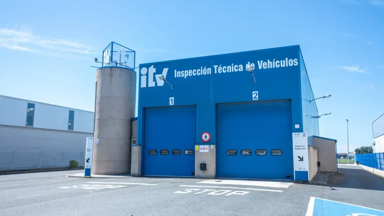 Edificio azul de ITV con dos puertas de garaje. Un coche listo para pasar la primera ITV.