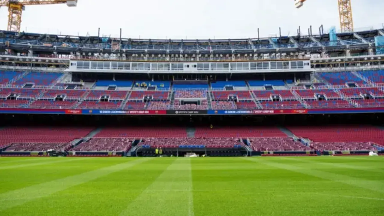 El estadio Spotify Camp Nou en obras, con grúas visibles. Las gradas rojas y azules esperan a los aficionados tras la renovación, cerca de la estación de metro.