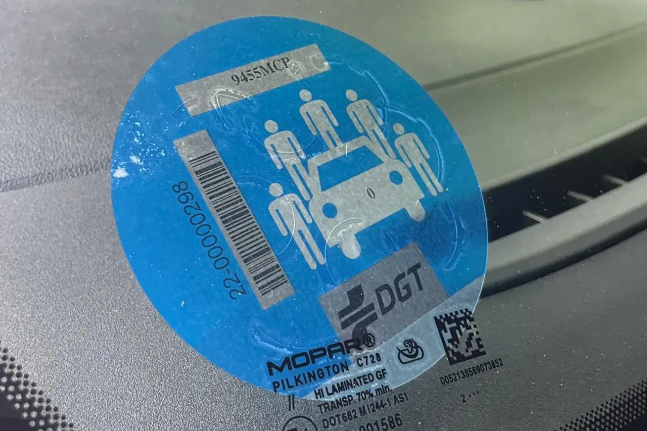 Pegatina azul con siluetas de personas y un coche, indicando la **señal v26**. Muestra un código de barras y el logo de DGT.