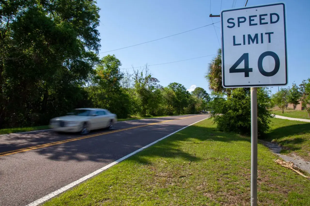 Señal de límite de velocidad de 40 en una carretera convencional. Un coche blanco pasa a gran velocidad.